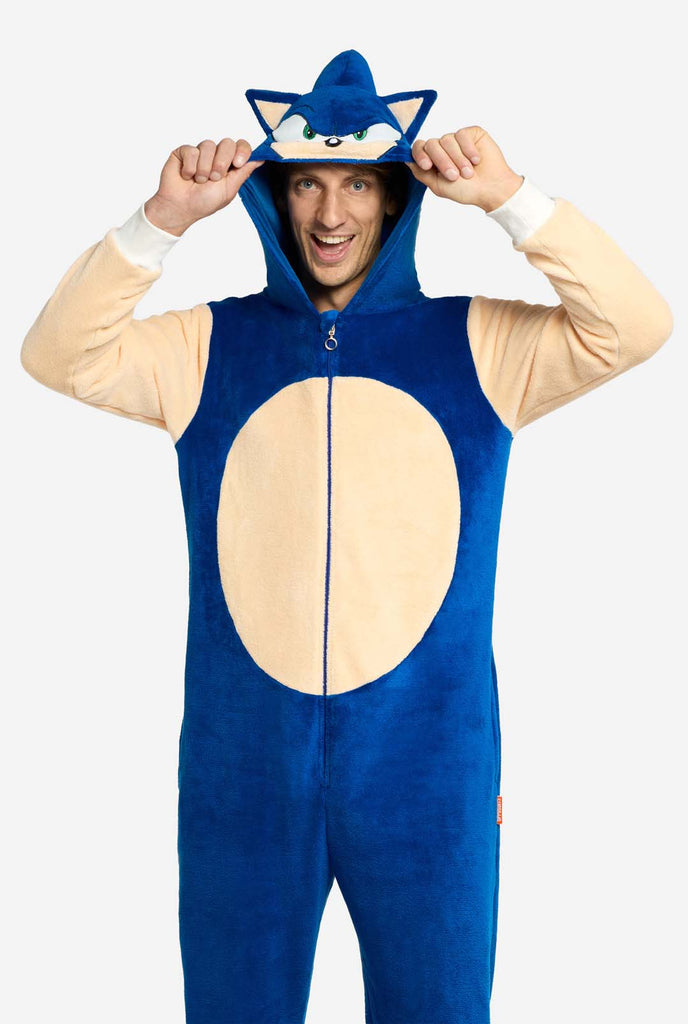 A man is wearing a playful blue and beige Sonic the Hedgehog-themed adult onesie from OppoSuits. The cozy onesie features a zip-up front and an attached hood designed to resemble Sonic’s iconic face, complete with ears and an expressive gaze. The blue body of the suit contrasts with a beige belly, mimicking Sonic's classic look. This fun, comfortable, and stylish onesie is perfect for lounging, themed parties, or cosplay events, bringing nostalgic video game vibes to any occasion.