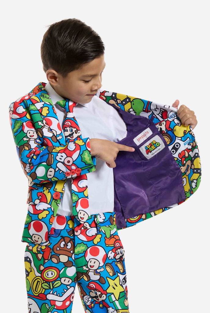 Image of kid wearing a Super Mario all over print suit, consisting of blazer, pants and tie. Main color is blue, but there is also yellow, red and white.