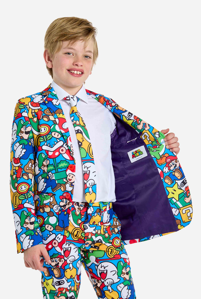 Image of teen wearing a Super Mario all over print shirt, consisting of blazer, pants and tie. Main color is blue, but there is also yellow, red and white.