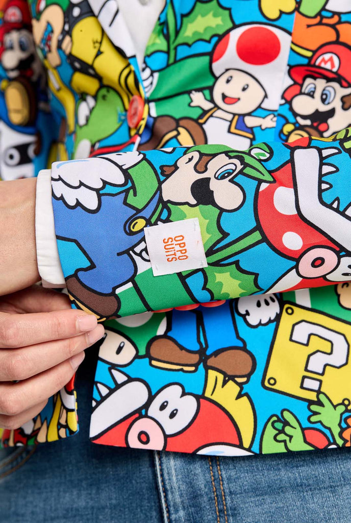 Woman wearing all-over print Super Mario blazer with iconic Super Mario characters. The base is light blue, but there is also yellow, red and white.