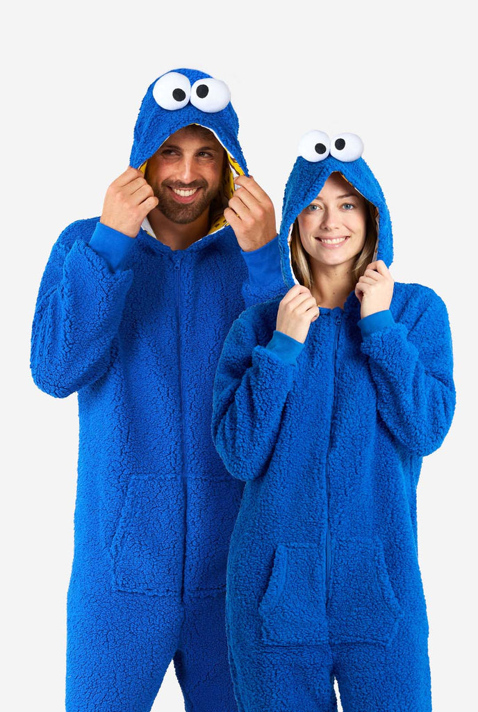 Man and Woman wearing blue pluche Cookie Monster Adult onesie for adults. Standing next to each other, holding hood with the hand.