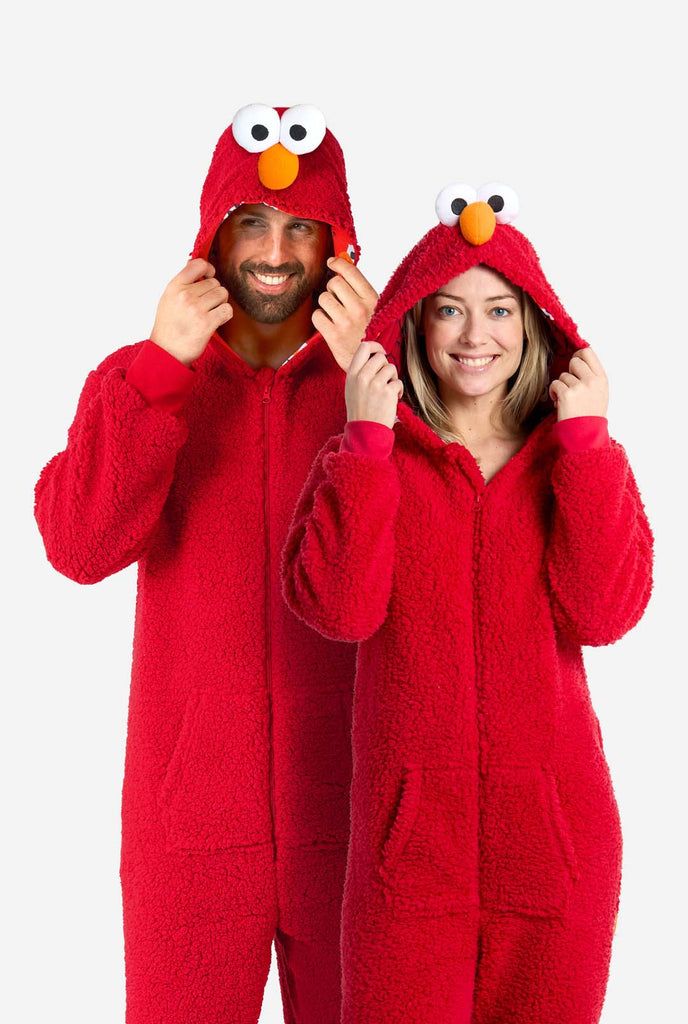 A man and a woman are dressed in a red Elmo-themed onesie. The overall design mimics the look of the Sesame Street character Elmo. The background is plain, putting focus on the costume.