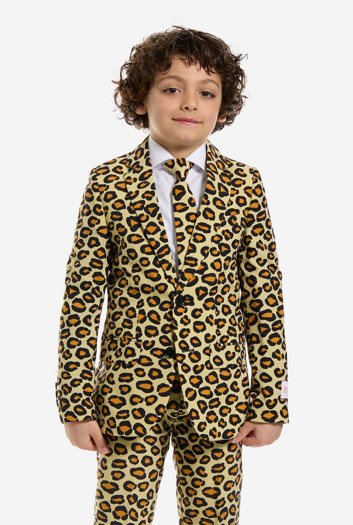 In this image, a kid is wearing a boys’ suit with all-over panther print and white shirt. The suit is beige with brown and black spotted panther print. Suits consists of jacket, pants and clip-on tie.