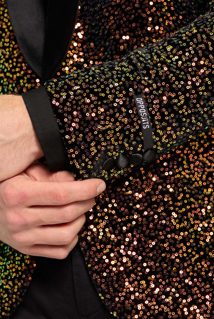 Man wearing blazer covered in with shimmering amber-colored sequins that reflect light in various shades of gold, copper, and green. Close up.