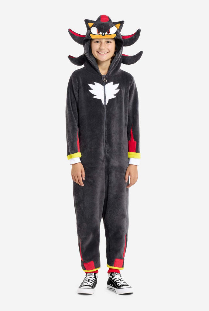 A kid wearing a plush black kids onesie inspired by the popular hedgehog character Shadow, featuring spiky red and black accents on the hood, a white chest emblem, and yellow wrist details. The onesie is made from soft fleece material, offering comfort and a playful design for cosplay, lounging, or themed events. Perfect for fans of gaming or animated characters. Full body image.