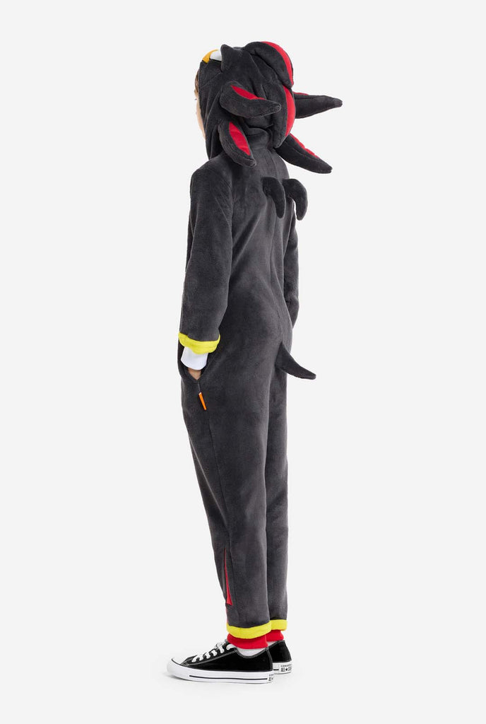 A kid wearing a plush black kids onesie inspired by the popular hedgehog character Shadow, featuring spiky red and black accents on the hood, a white chest emblem, and yellow wrist details. The onesie is made from soft fleece material, offering comfort and a playful design for cosplay, lounging, or themed events. Side view. Perfect for fans of gaming or animated characters.