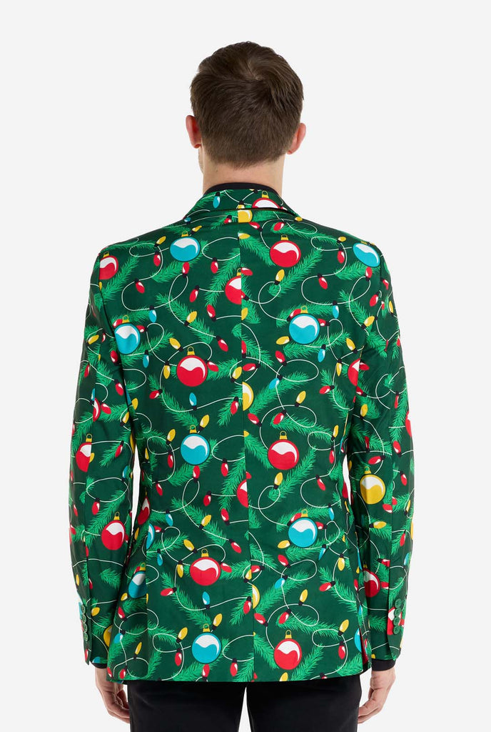 Man wearing green Christmas blazer for men with decorated Christmas tree print. Man also wearing a black pants and black men's shirt. View from the back.