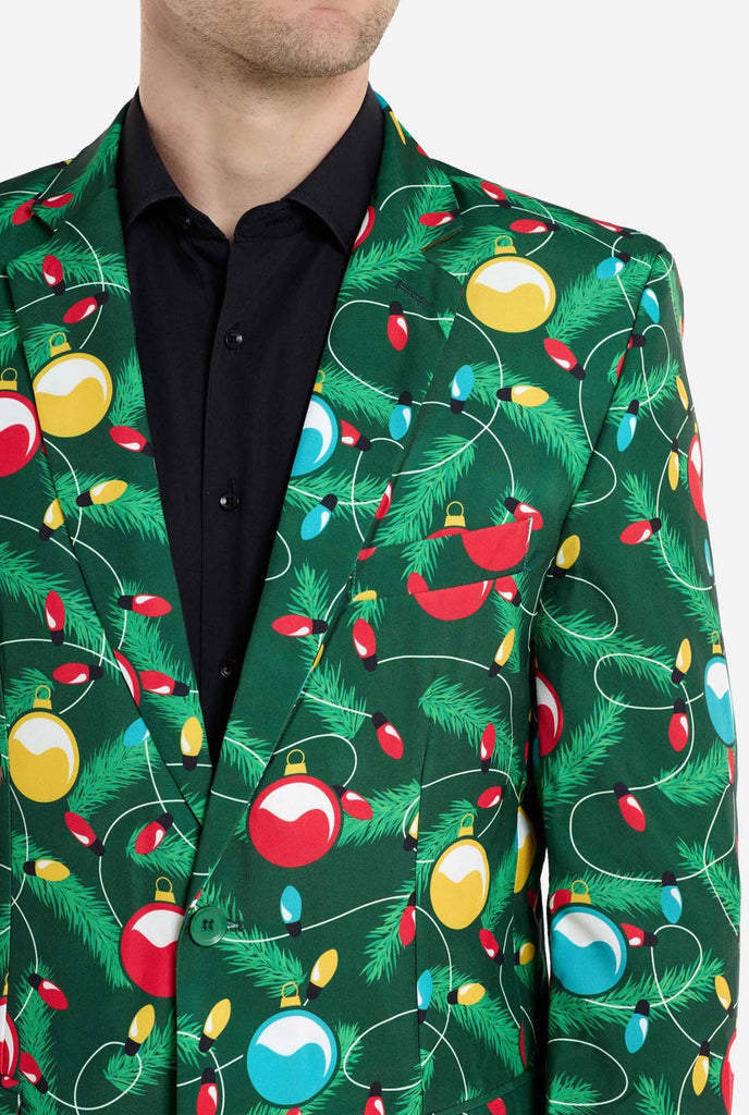 Man wearing green Christmas blazer for men with decorated Christmas tree print. Man also wearing a black pants and black men's shirt. Chest close up.