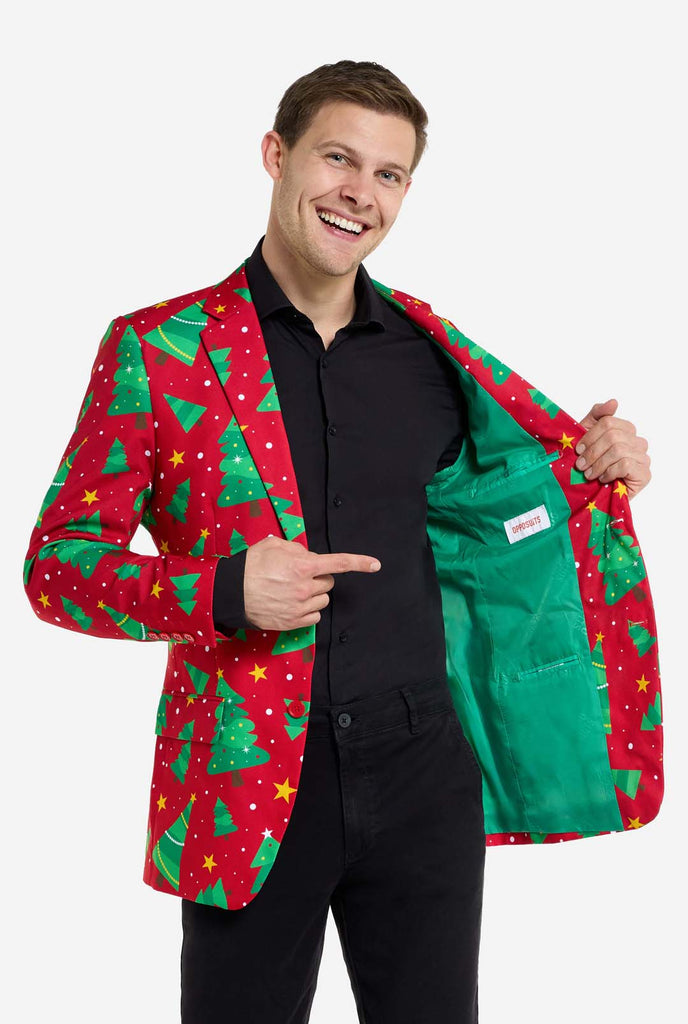 Man wearing red Christmas blazer for men with Christmas trees and stars print. Man also wearing a black pants and black men's shirt. Showing green inside of the jacket.