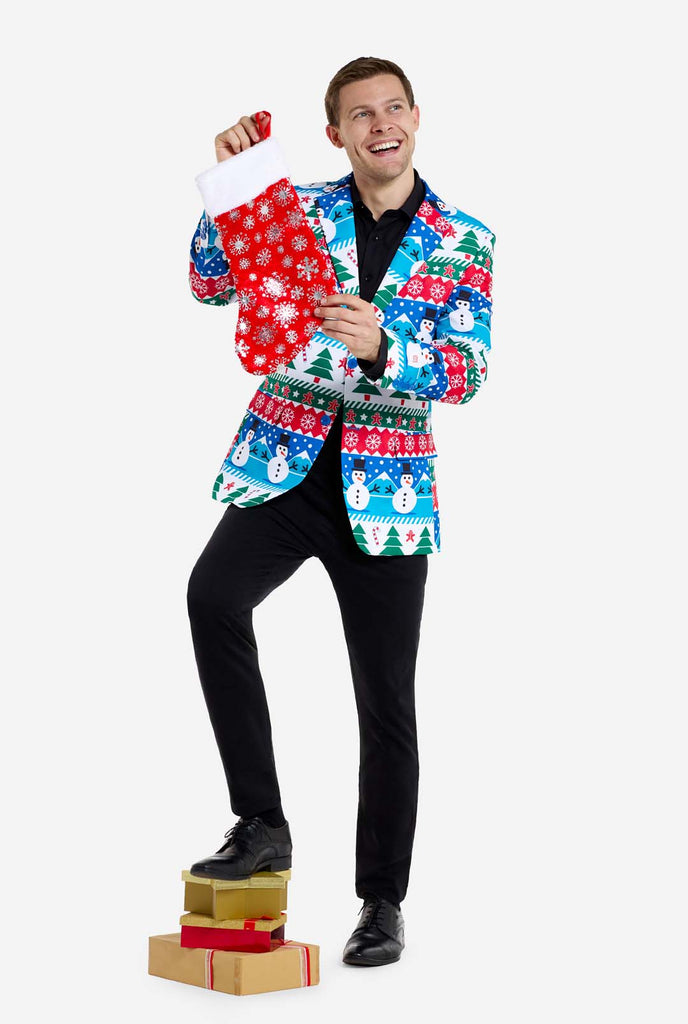 Man wearing Christmas blazer for men with Christmas winter figures. Man also wearing a black pants and black men's shirt. Holding Christmas sock.