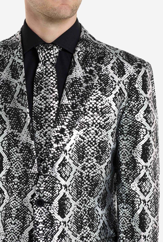 A man is wearing an eye-catching silver and black snake-print suit by OppoSuits. The striking suit features a bold snakeskin pattern, offering a sleek, fashionable look perfect for parties, events, or making a daring fashion statement. The men suit is paired with a black dress shirt and a matching snake-print tie, adding a sophisticated edge to the overall ensemble. Chest close up.