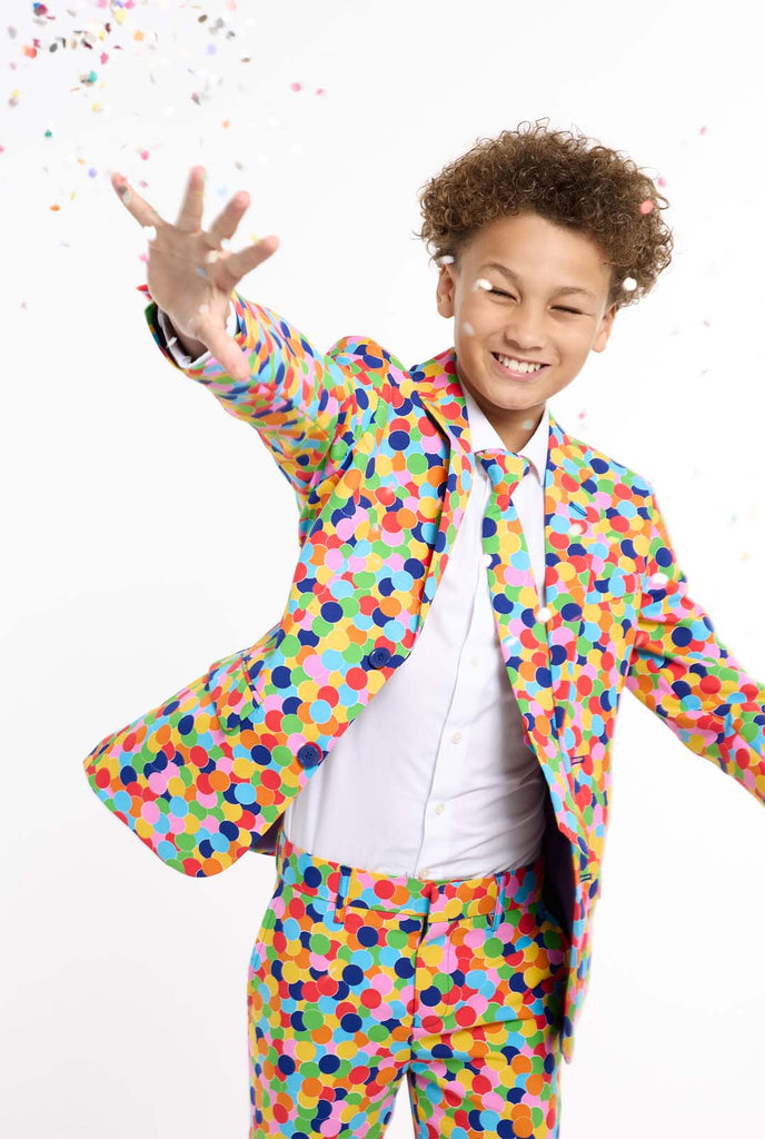 In this image, a kid is wearing a colorful, polka-dotted suit. The suit has a bright pattern with circles in various colors including orange, yellow, pink, green, blue, and red, arranged in a confetti-like style.