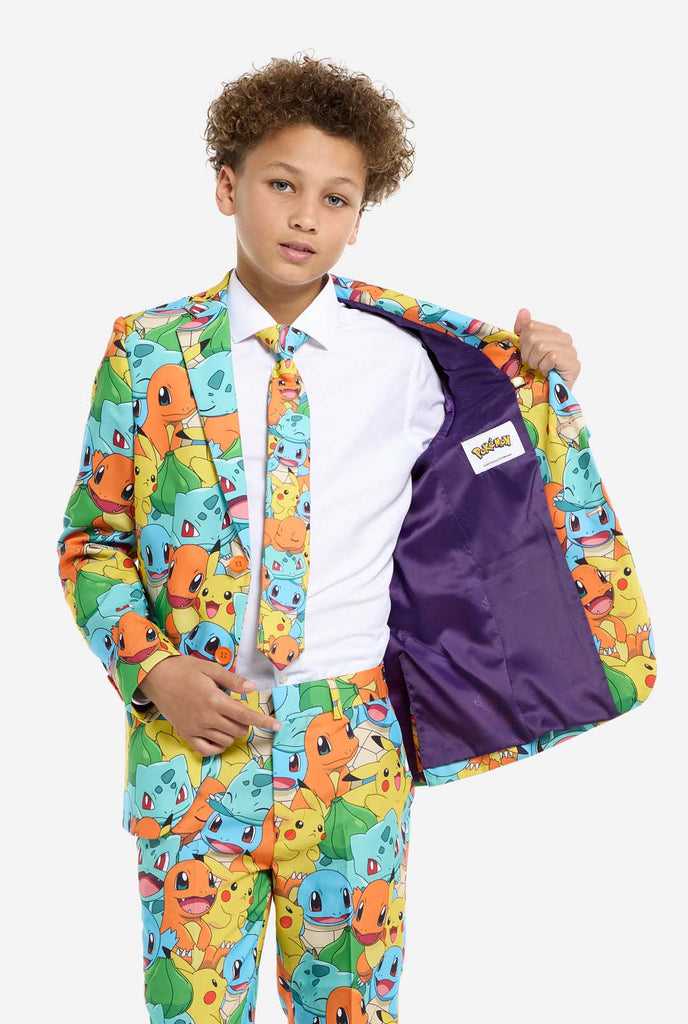 Teen wearing formal multi color suit with all-over Pokemon print. The suit contains the characters Pikachu, Bulbasaur, Charmander and Squirtle.