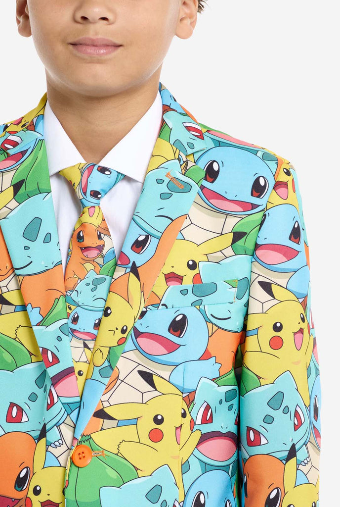 Teen wearing formal multi color suit with all-over Pokemon print. The suit contains the characters Pikachu, Bulbasaur, Charmander and Squirtle.