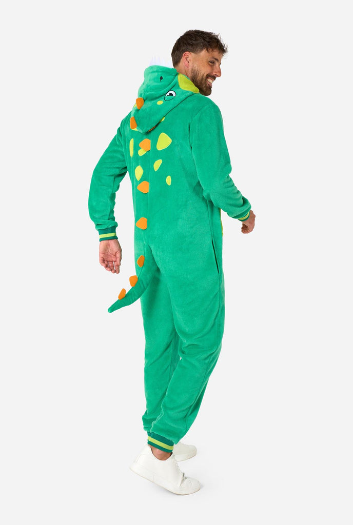 A man is wearing a green dinosaur adult onesie featuring playful hood details and cozy, soft material, perfect for lounging or costume events. He is standing sideways and showing the ack of the onesie.