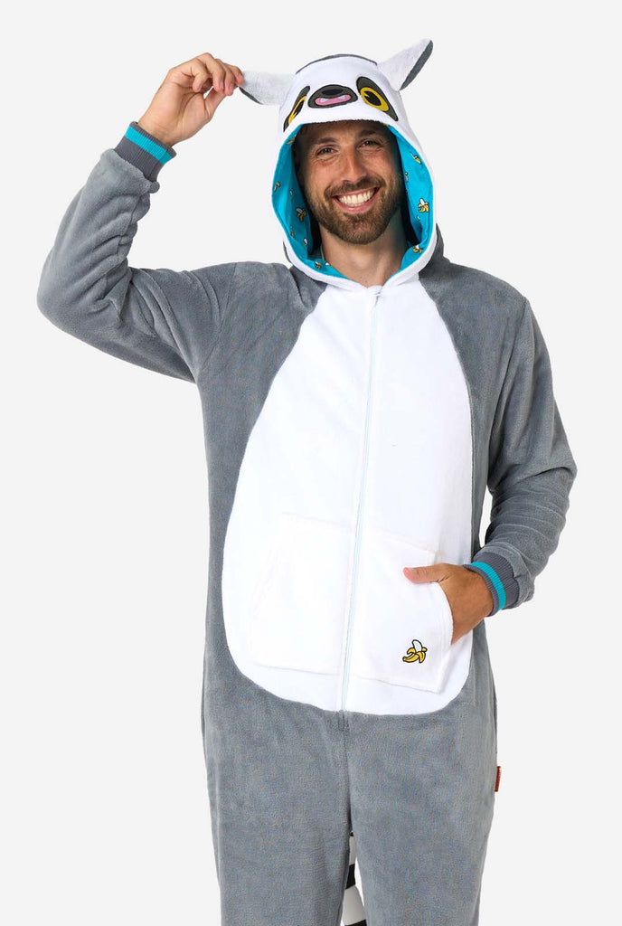 A man is wearing a grey and white lemur adult onesie featuring playful hood details and cozy, soft material, perfect for lounging or costume events. Including black and white tail. The man is holding the hood and is smiling in the camera.