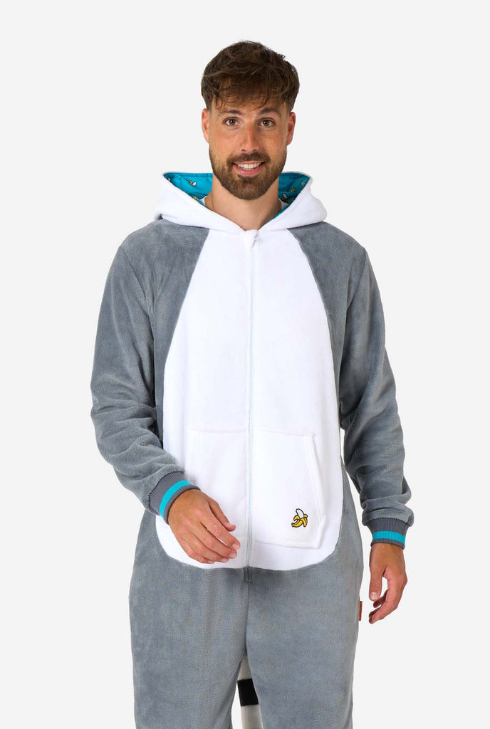 A man is wearing a grey and white lemur adult onesie featuring playful hood details and cozy, soft material, perfect for lounging or costume events. Including black and white tail. The hood is down on his back.