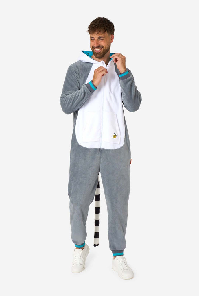 A man is wearing a grey and white lemur adult onesie featuring playful hood details and cozy, soft material, perfect for lounging or costume events. Including black and white tail. Full body image with the hood down on his back and visible tail.