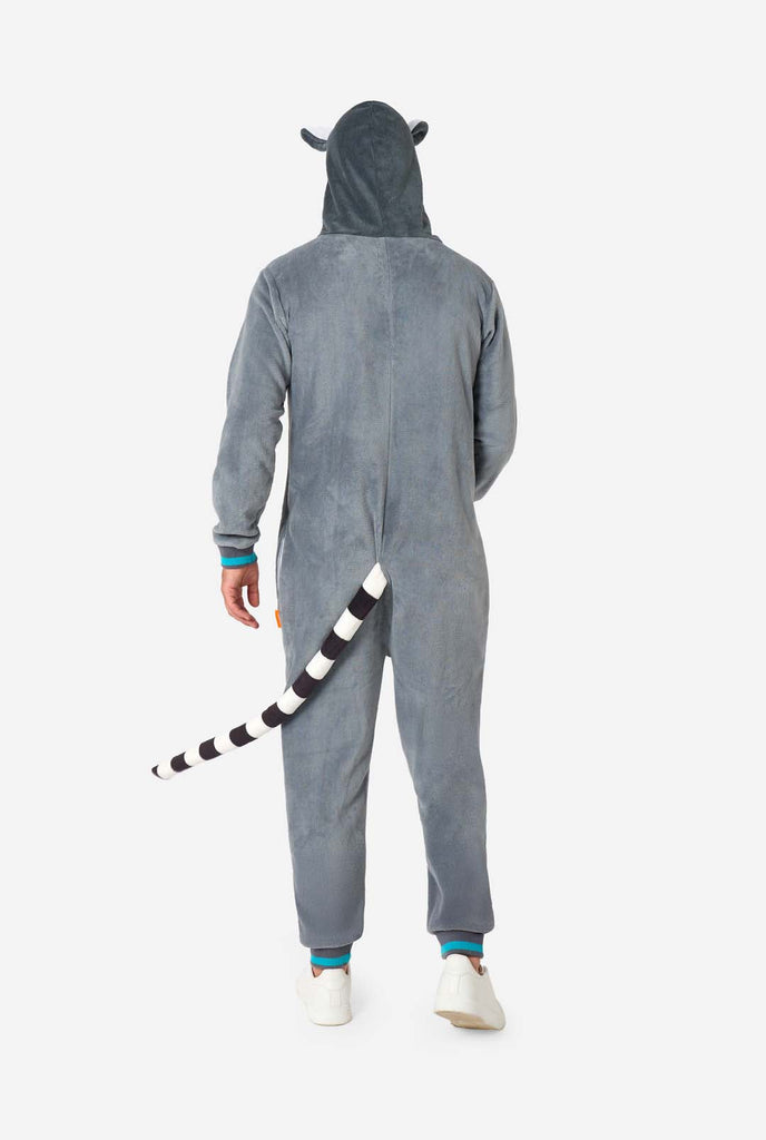 A man is wearing a grey and white lemur adult onesie featuring playful hood details and cozy, soft material, perfect for lounging or costume events. Including black and white tail. Full body image showing the back of the onesie.