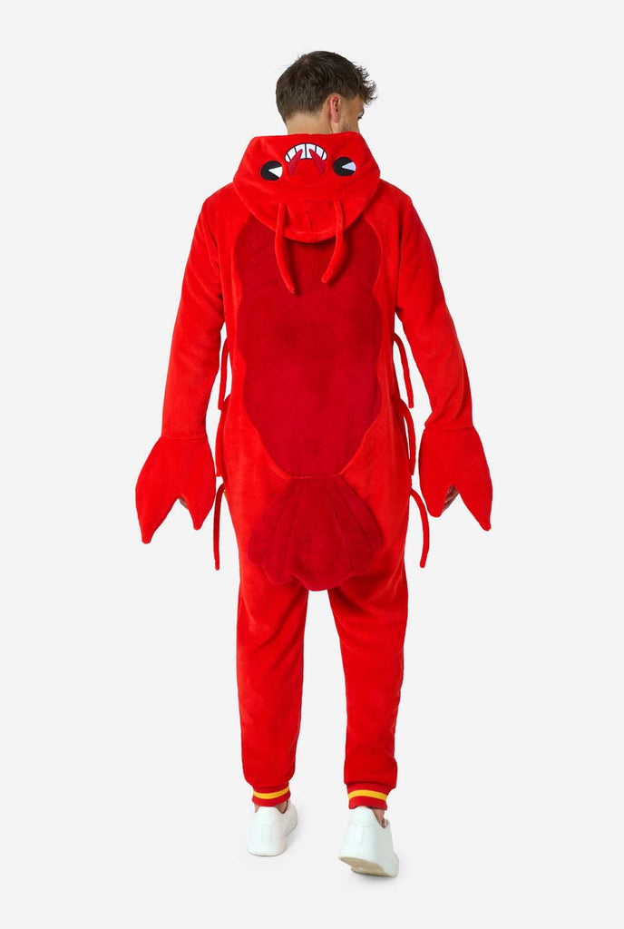 A man is wearing a bright red lobster-themed adult onesie featuring playful hood details and cozy, soft material, perfect for lounging or costume events. including stitched gloves as claws. View from the back showing tail and hood down on his back.