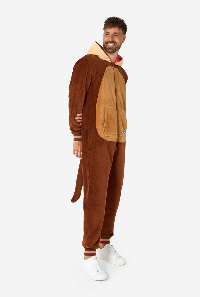 A smiling man is wearing a brown adult onesie designed as an otter. The onesie features a hood with ears, a cute face, and playful otter details, perfect for cozy lounging or costume parties. Full body image with the man standing and looking sideways. 