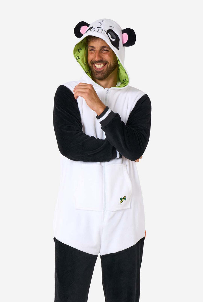 A smiling man wearing a panda-themed adult onesie. This cozy onesie features black and white panda colors with a playful hood showcasing panda ears and a cute face. Perfect for lounging or fun costume occasions.