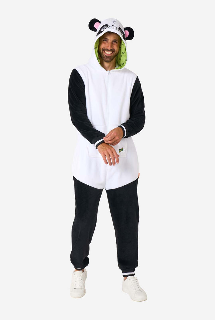 A smiling man wearing a panda-themed adult onesie. This cozy onesie features black and white panda colors with a playful hood showcasing panda ears and a cute face. Perfect for lounging or fun costume occasions. Full body image.