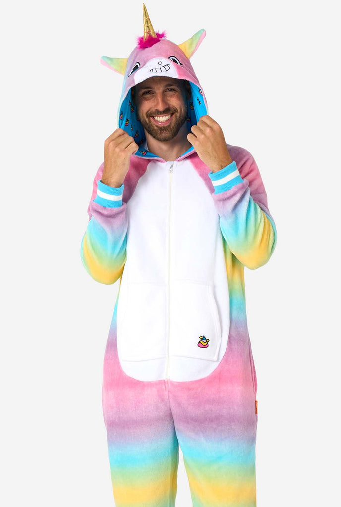 A cheerful man wearing a colorful adult onesie designed as a rainbow unicorn. The onesie features a vibrant gradient of pastel colors, a golden horn, and playful unicorn details, perfect for cozy lounging or costume parties.