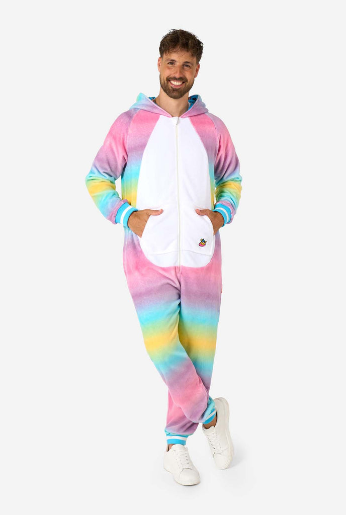 A man wearing a colorful adult onesie designed as a rainbow unicorn. The onesie features a vibrant gradient of pastel colors, a golden horn, and playful unicorn details, perfect for cozy lounging or costume parties. The hood is lying flat on his back. Full body image.