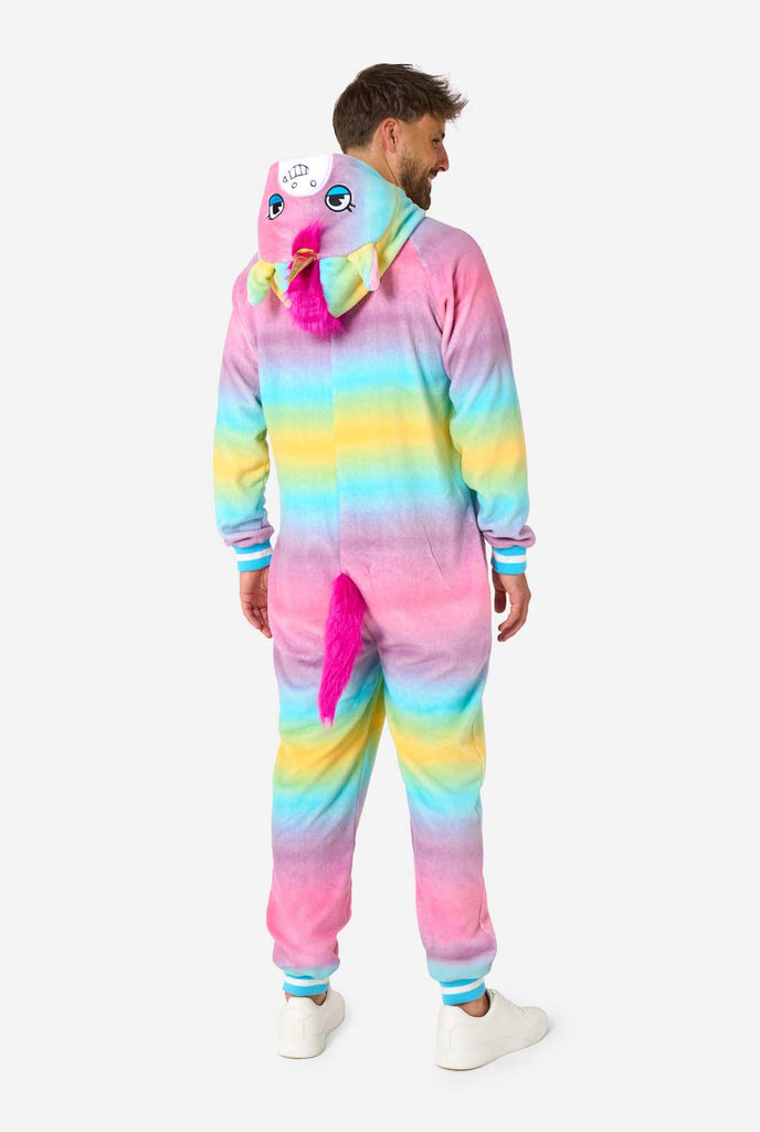 A man wearing a colorful adult onesie designed as a rainbow unicorn. The onesie features a vibrant gradient of pastel colors, a golden horn, and playful unicorn details, perfect for cozy lounging or costume parties. The hood is lying flat on his back. View from the back.