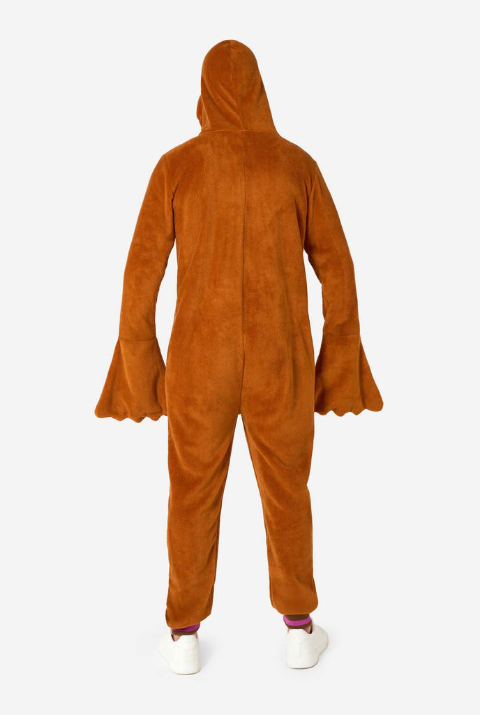 A cheerful man wearing a brown adult onesie designed as a walrus. The onesie features a hood with fangs, stitched gloves resembling paws, and playful walrus details, perfect for cozy lounging or costume parties. Full body image view from the back.