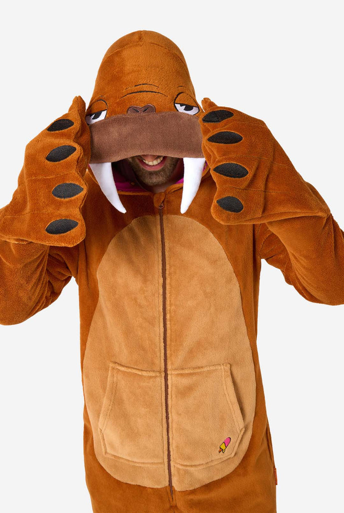 A cheerful man wearing a brown adult onesie designed as a walrus. The onesie features a hood with fangs, stitched gloves resembling paws, and playful walrus details, perfect for cozy lounging or costume parties. Upper body close up.