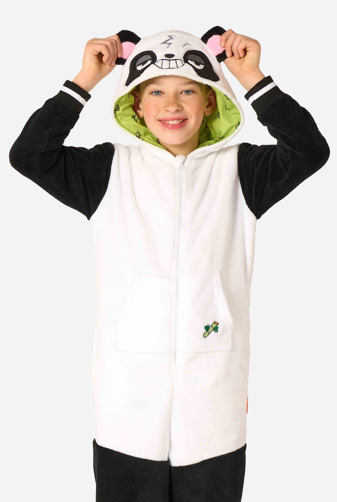 A smiling kid wearing a panda-themed kids onesie. This cozy onesie features black and white panda colors with a playful hood showcasing panda ears and a cute face. Perfect for lounging or fun costume occasions.