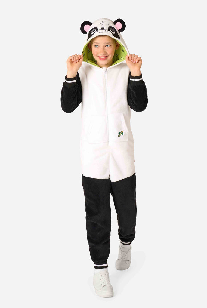 A smiling kid wearing a panda-themed kids onesie. This cozy onesie features black and white panda colors with a playful hood showcasing panda ears and a cute face. Perfect for lounging or fun costume occasions. Full body image.