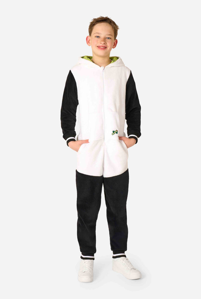 A smiling kid wearing a panda-themed kids onesie. This cozy onesie features black and white panda colors with a playful hood showcasing panda ears and a cute face. Perfect for lounging or fun costume occasions. Full body with the hood down.