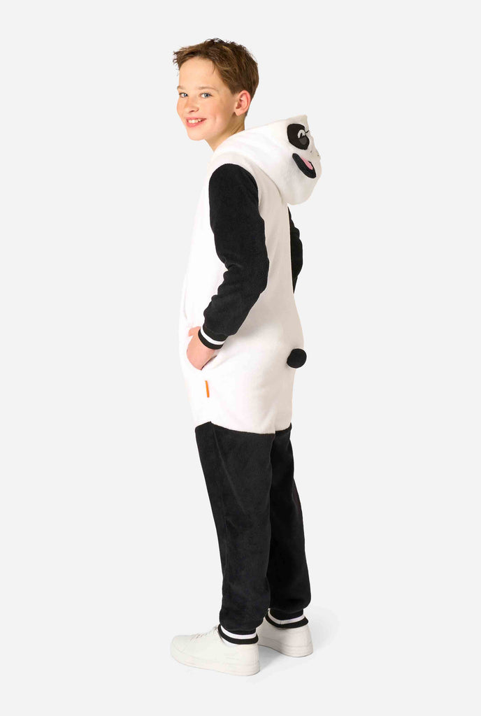 A smiling kid wearing a panda-themed kids onesie. This cozy onesie features black and white panda colors with a playful hood showcasing panda ears and a cute face. Perfect for lounging or fun costume occasions. Full body side image, hood down.