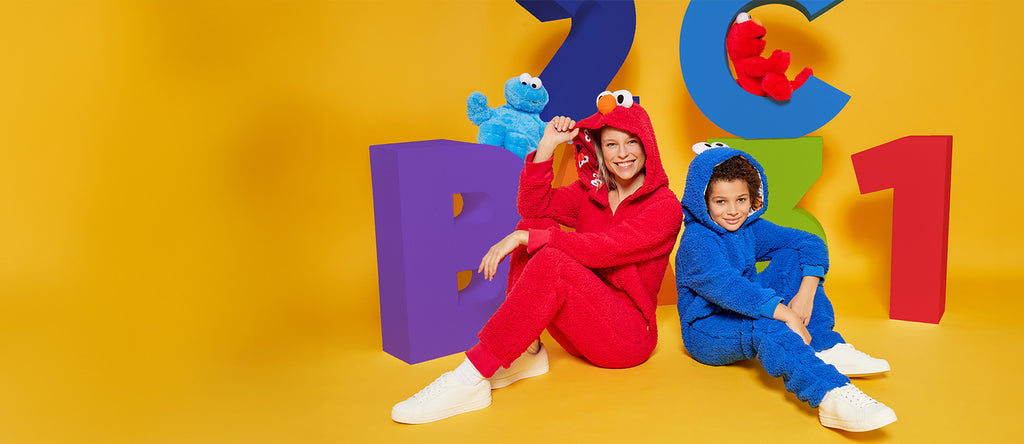 Woman wearing Elmo onesie and kid wearing Cookie monster onesie.