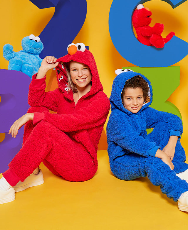 Woman wearing Elmo onesie and kid wearing Cookie monster onesie.